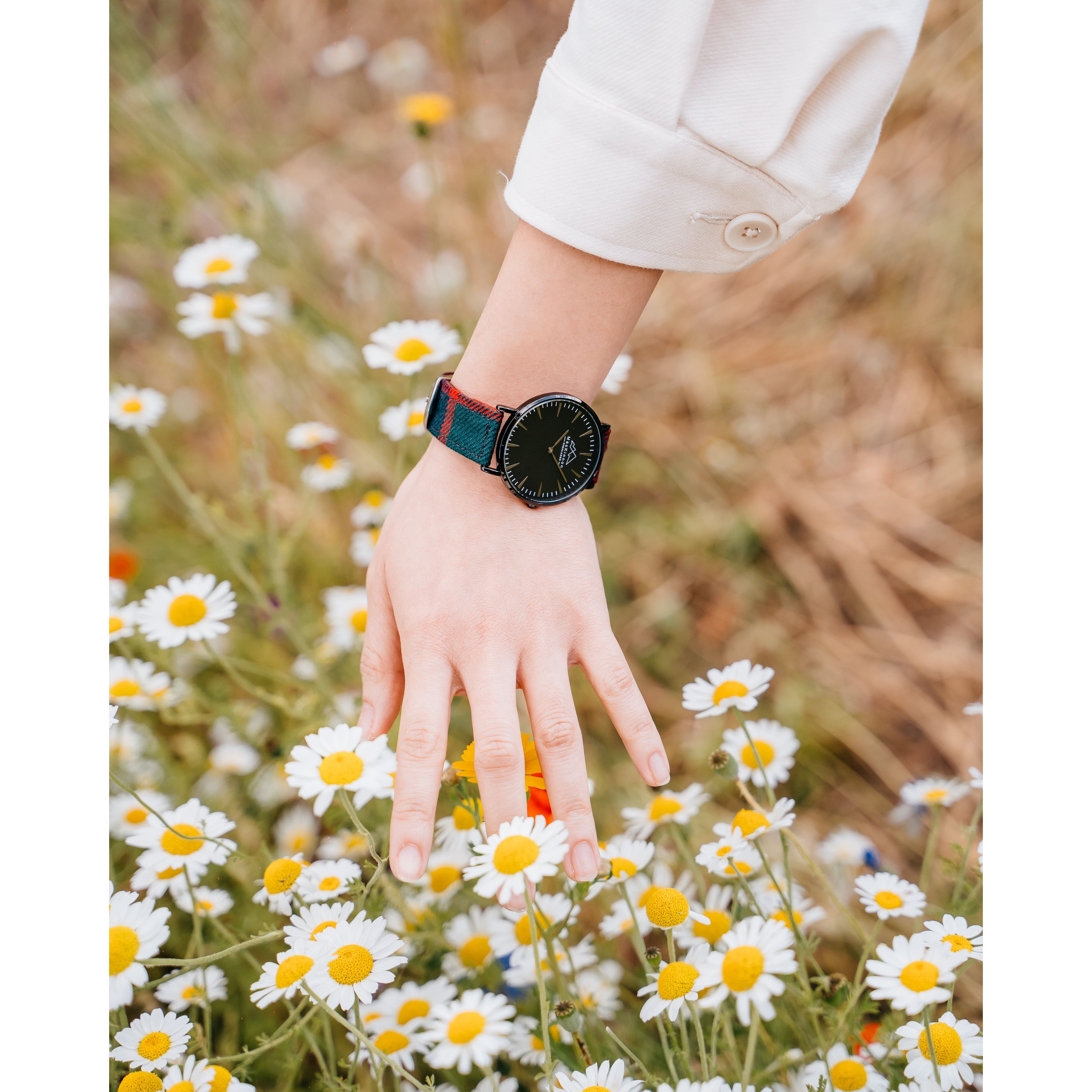 A woman touching flowers with her hand with a custom tartan watch on her arm